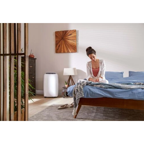Qlima portable air conditioner in a bedroom next to a bed and side table.