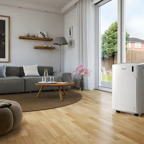 The De'Longhi Pinguino PAC EM82K.1 portable air conditioner operating inside a modern living room next to a glass sliding patio door, on a light oak wood laminate floor.